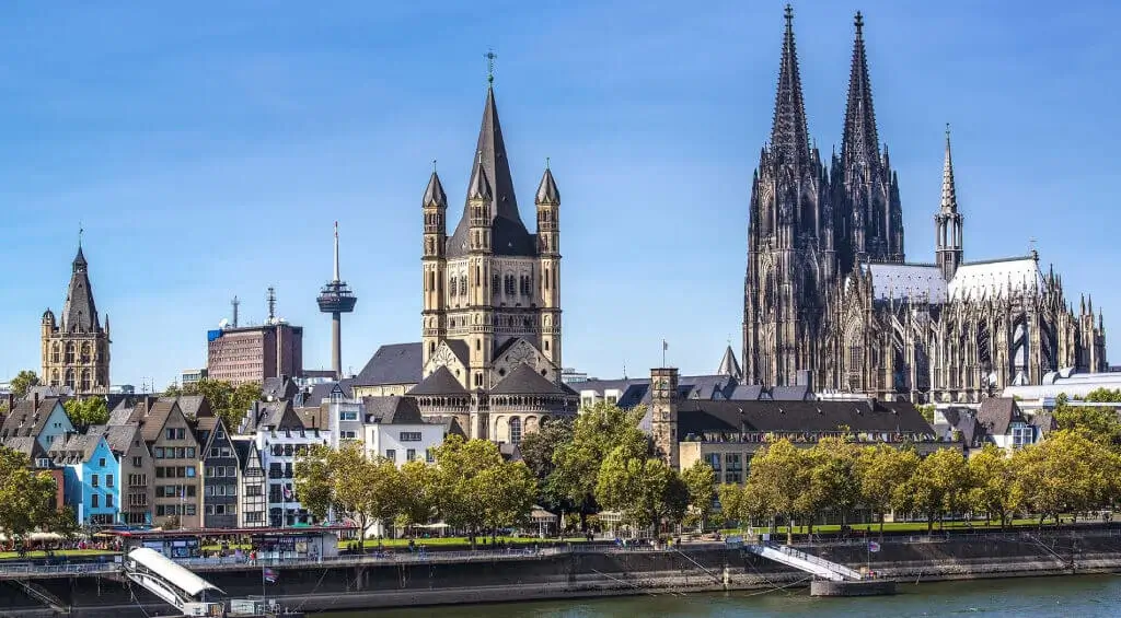 Study in Germany – Sunset view of Cologne’s famous cathedral and the Hohenzollern Bridge, beautifully illuminated against a vibrant purple sky.